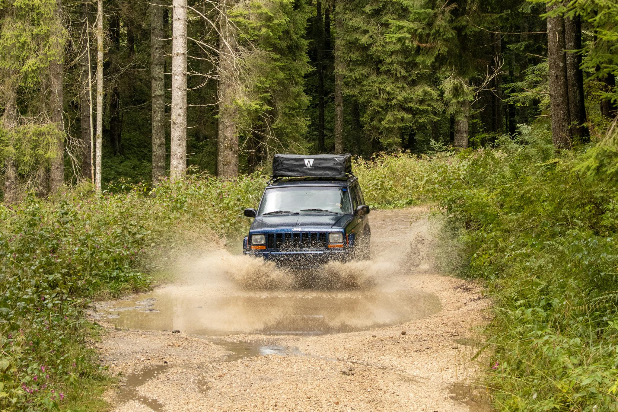 4x4 vehicle splashing through a muddy trail in a dense forest in Asiago, Italy.