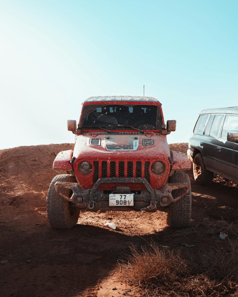 Front view of a red Jeep Wrangler on a dusty off-road trail under a clear blue sky.