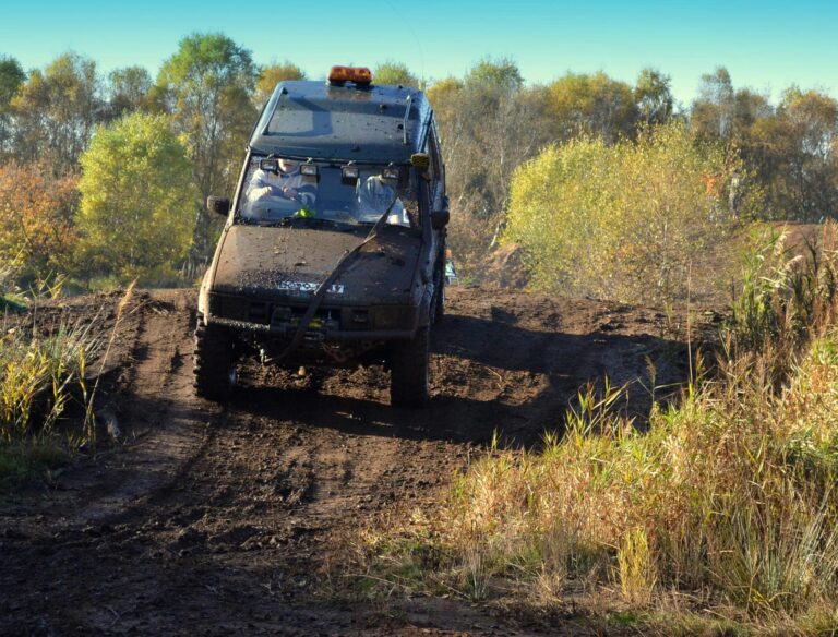 Off-road vehicle navigating muddy tracks in a forest setting during daytime adventure.