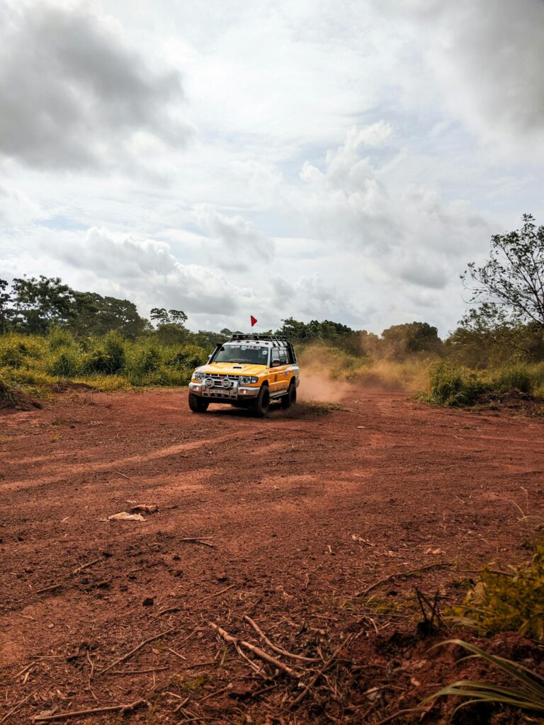 Yellow off-road vehicle drifting on a dirt trail amidst lush greenery during daytime.